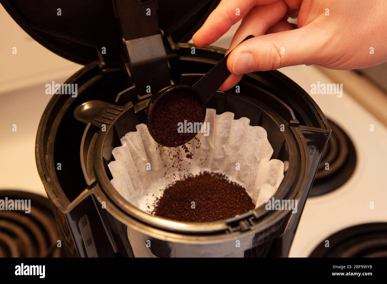 pouring a scoop of coffee grinds into a paper filter in a coffee maker Stock Photo