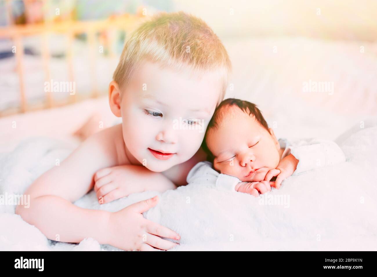 Happy little brother with newborn baby lying in a bed together, kissing