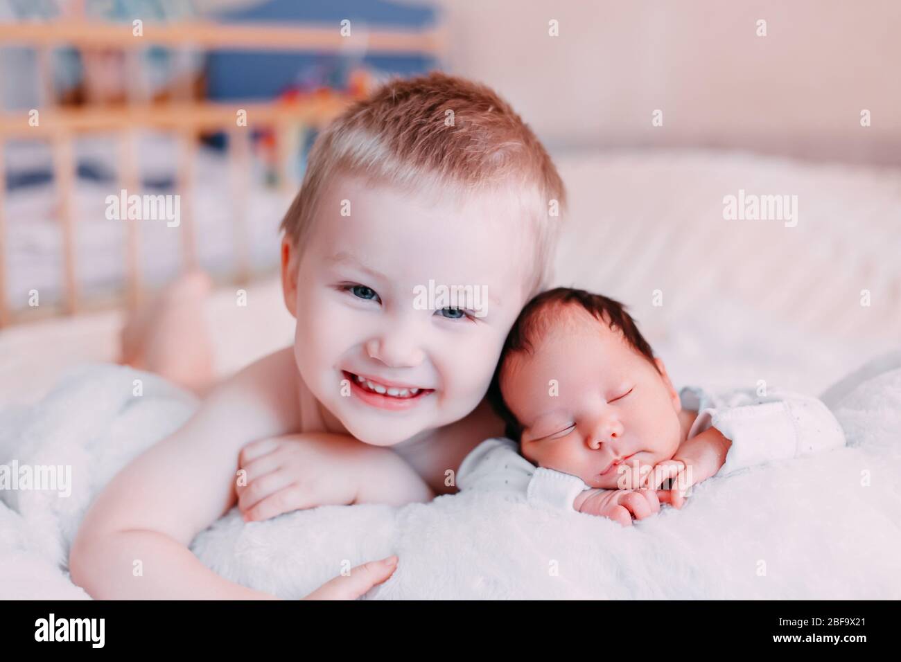 Happy little brother with newborn baby lying in a bed together, kissing