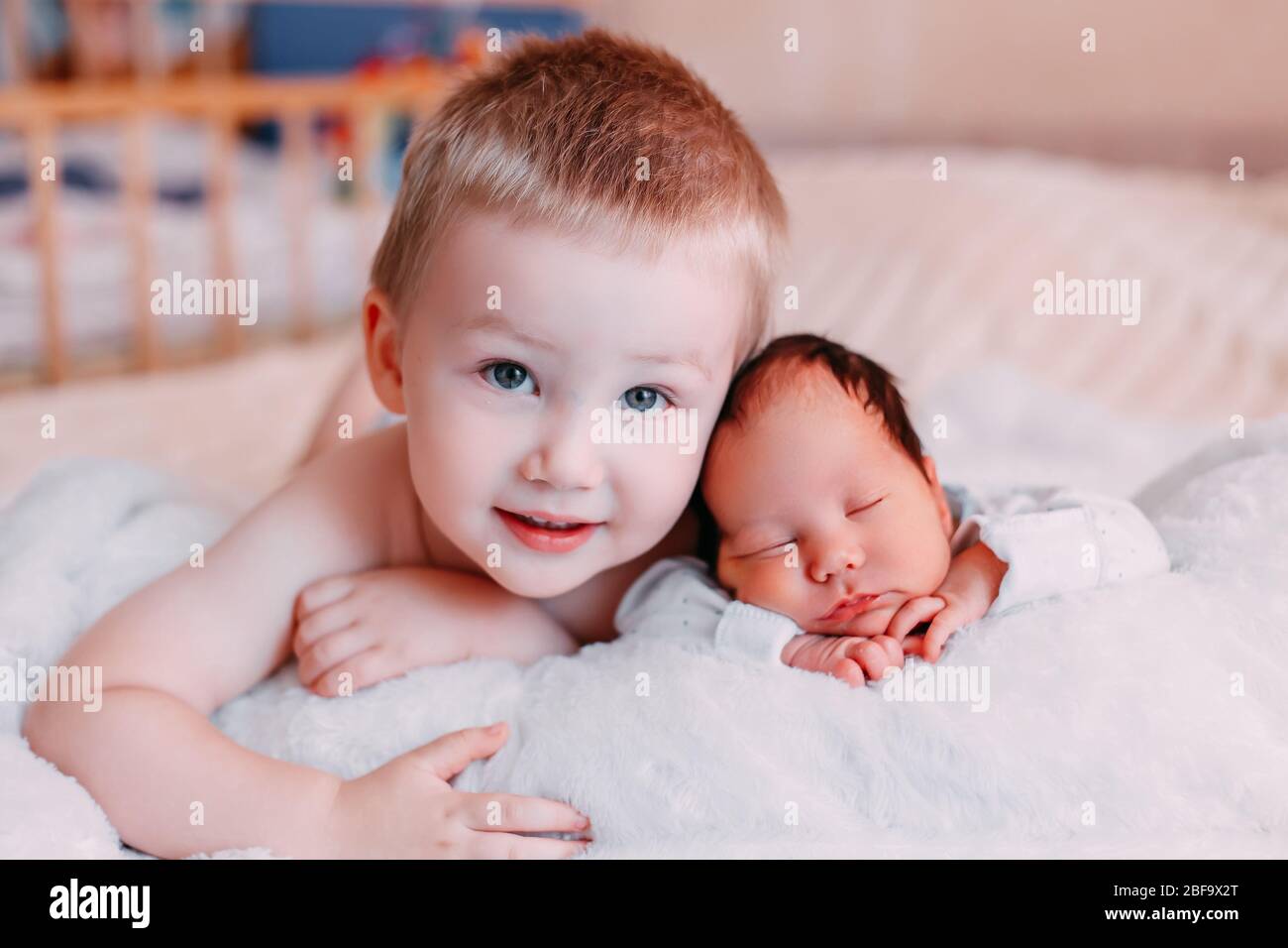 Happy little brother with newborn baby lying in a bed together, kissing