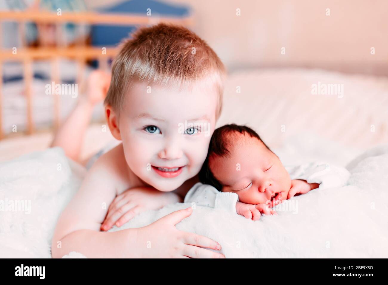 Happy little brother with newborn baby lying in a bed together, kissing