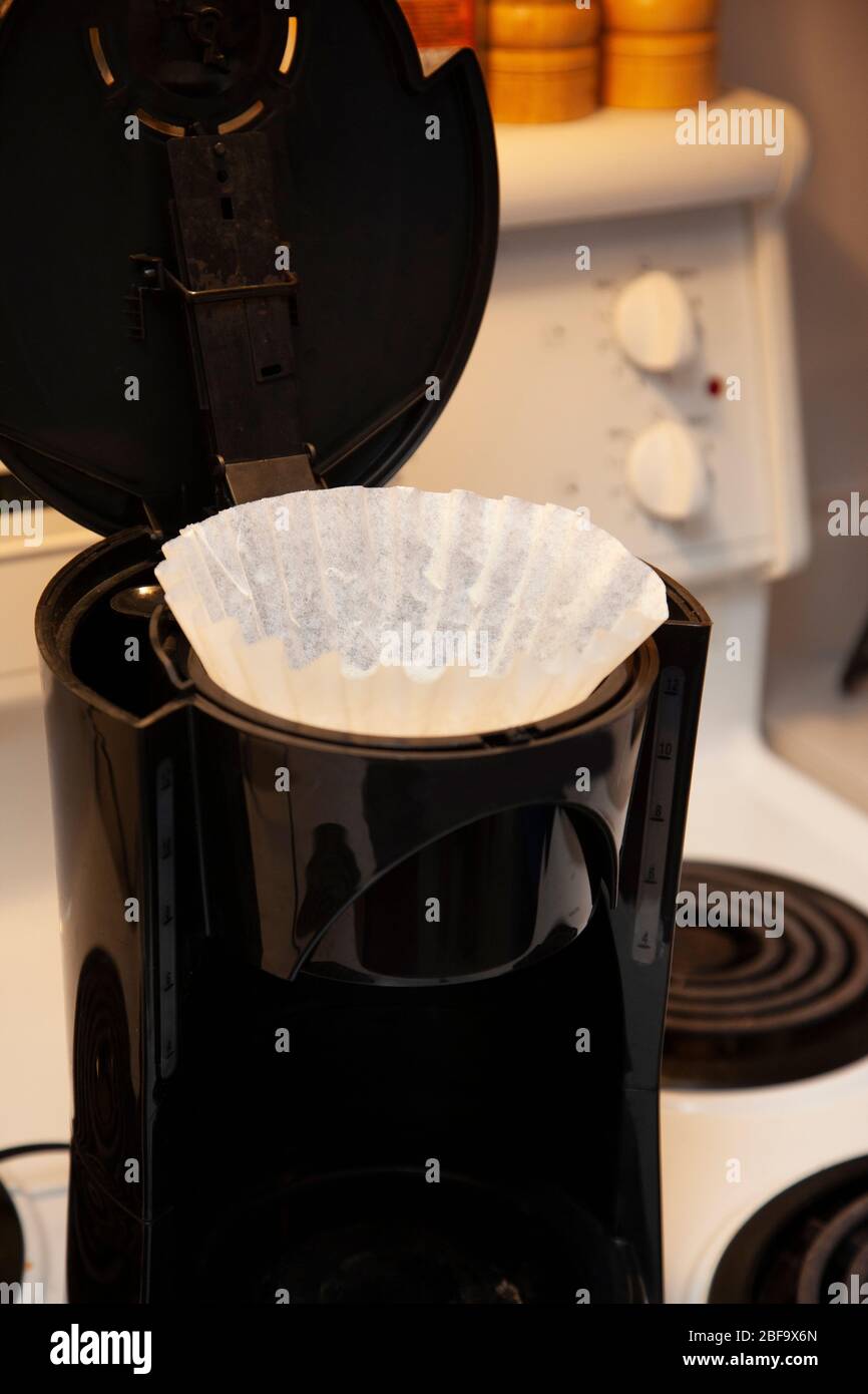 a white paper filter sitting in the top of a drip coffee maker on the stove Stock Photo