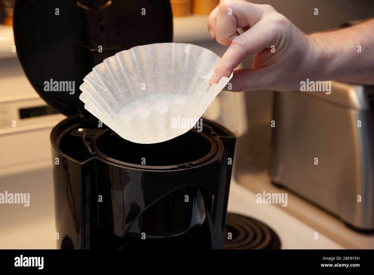 a hand puts a white paper filter into the top of a drip coffee maker Stock Photo