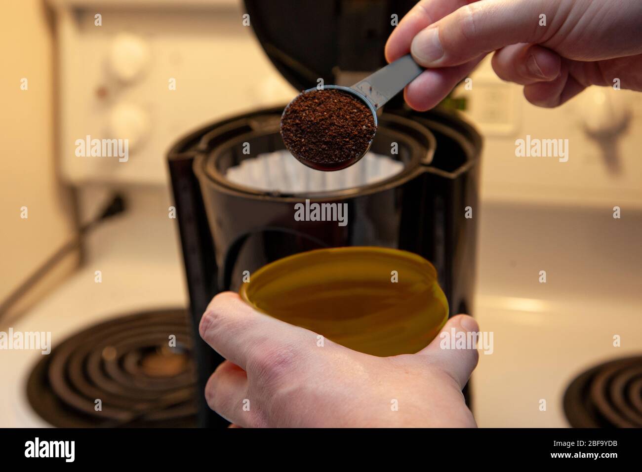 a hand measures a scoop of coffee grinds into a paper filter for coffee making Stock Photo