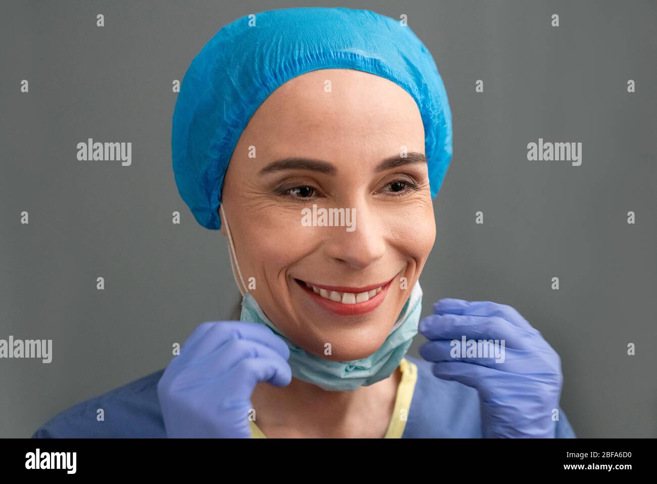 Female medical worker smiles removing surgical mask Stock Photo