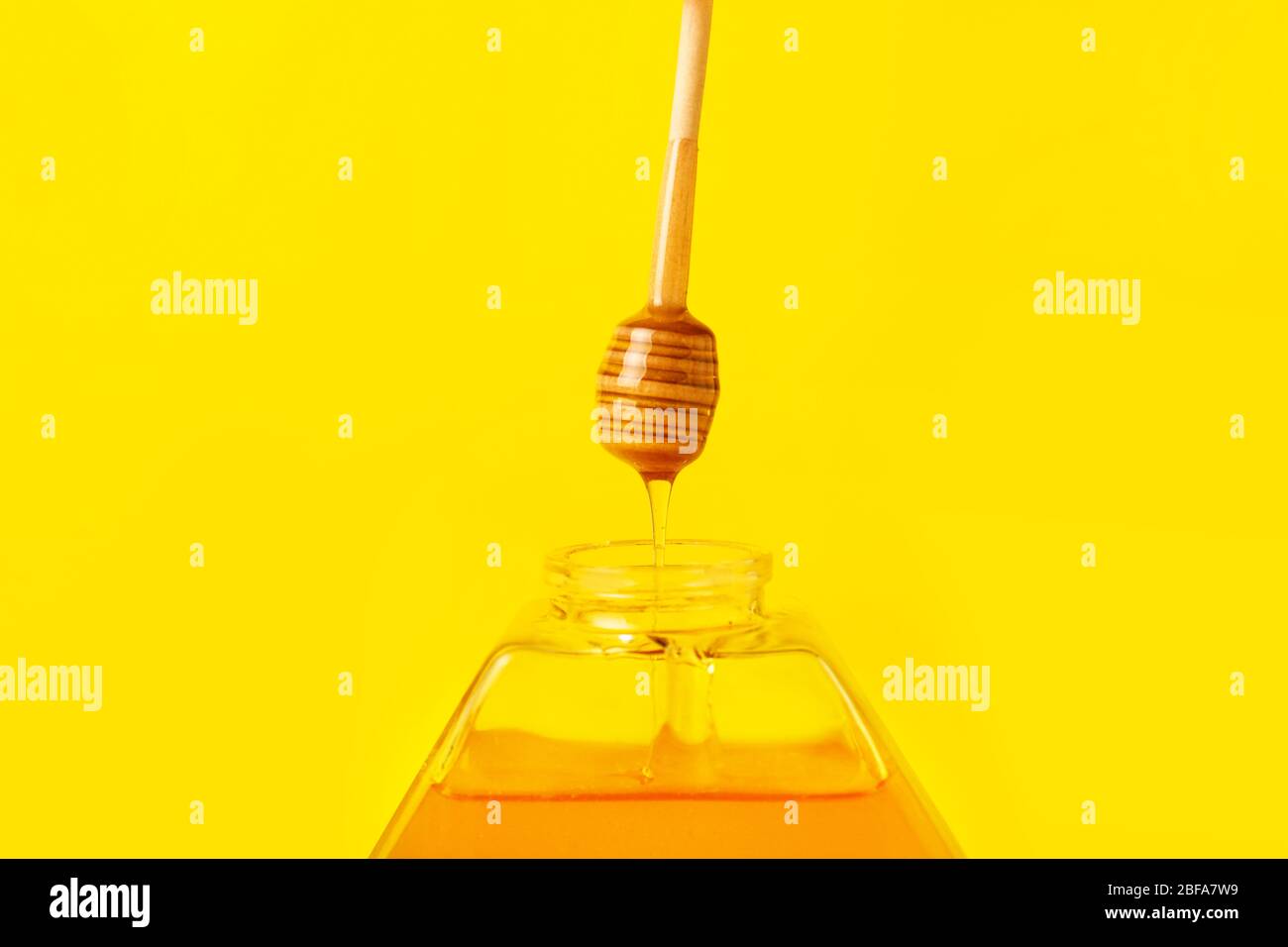 Honey dripping from dipper into jar on color background Stock Photo - Alamy