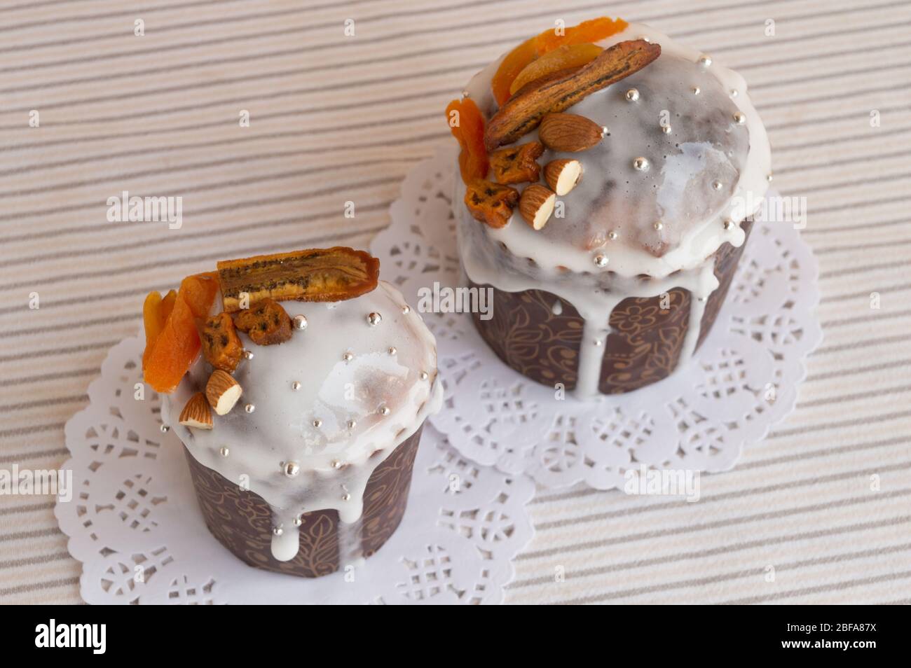 Top view of Traditional Orthodox Easter kulich. Two stylish delicious cake on the white napkin decorated by dried bananas, orange apricots, almonds an Stock Photo