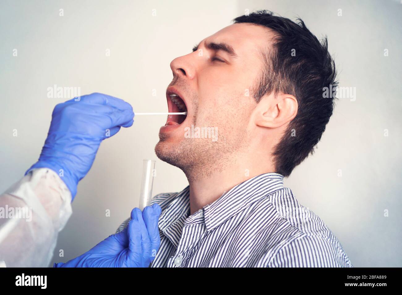 Doctor Doing Coronavirus covid 19 Test For male Patient. Taking a saliva sample from a man. DNA test. Collection of mucus from the throat for research Stock Photo