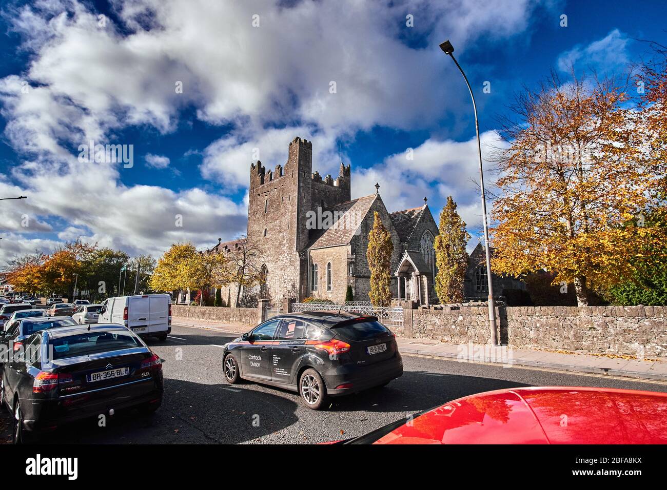 Street view of the Holy Trinity Abbey Church, Adare, Co. Limerick in October autumn with cars driving on busy road Stock Photo
