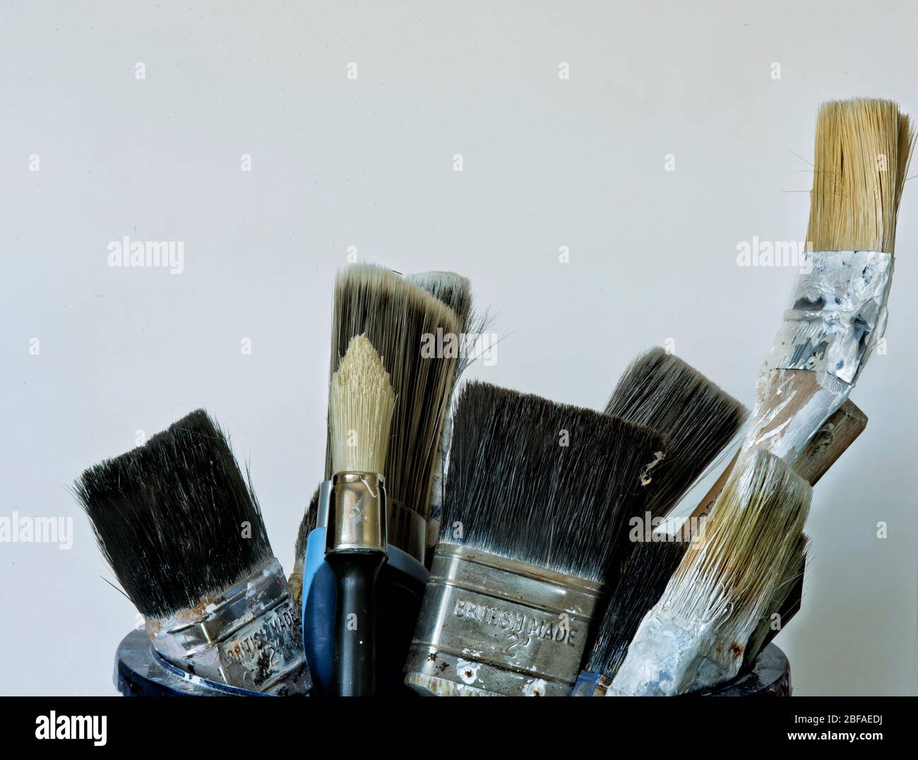 Used paint brushes standing in a paint holder bucket. against a white