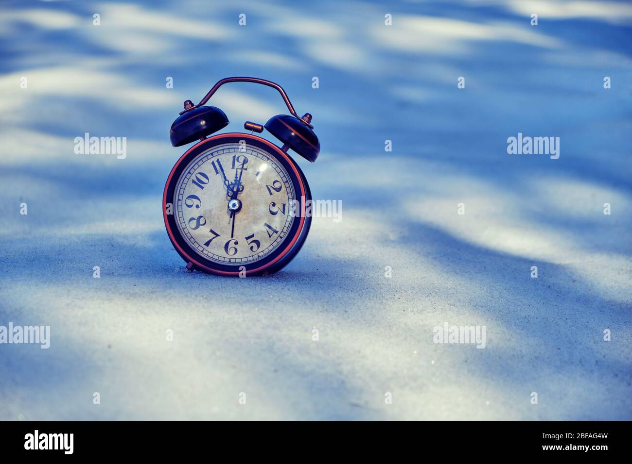 Old retro alarm clock in the snow in the forest with Sunny bunnies