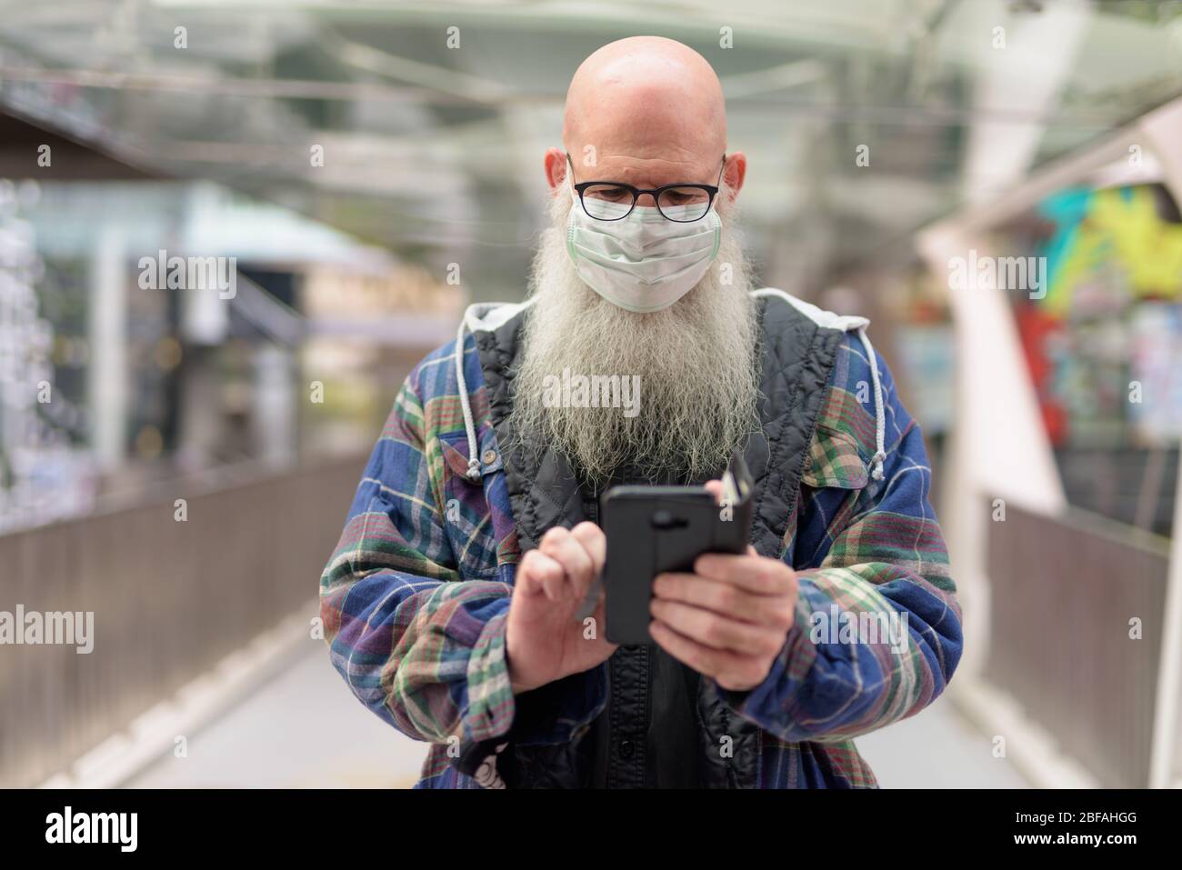 Mature bald bearded man with mask using phone in the city Stock Photo -  Alamy