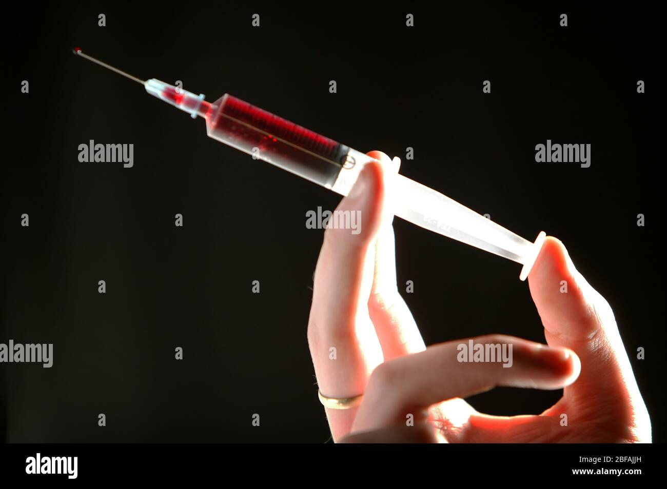 Hand gently squeezing a hypodermic syringe held pointing upwards to