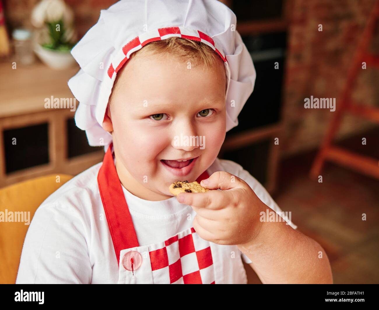 Little fat boy is eating a cake at home kitchen. Happy kids and childhood concept. Child's obesity concept. Stock Photo