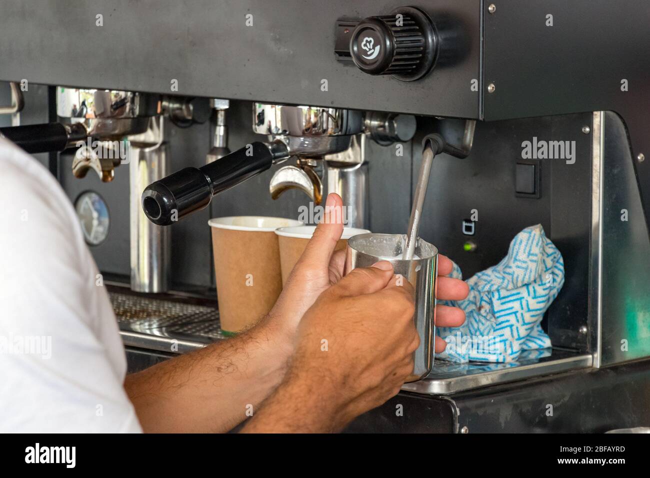 Male barista hands steaming milk preparing a take away cappuccino Stock Photo