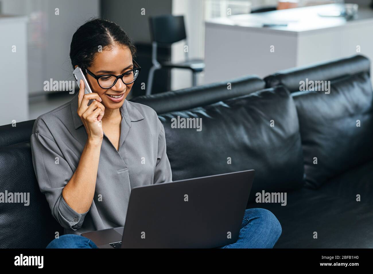 Beautiful woman using a smartphone having phone call from her apartment. Businesswoman enjoying conversation sitting on a couch. Stock Photo