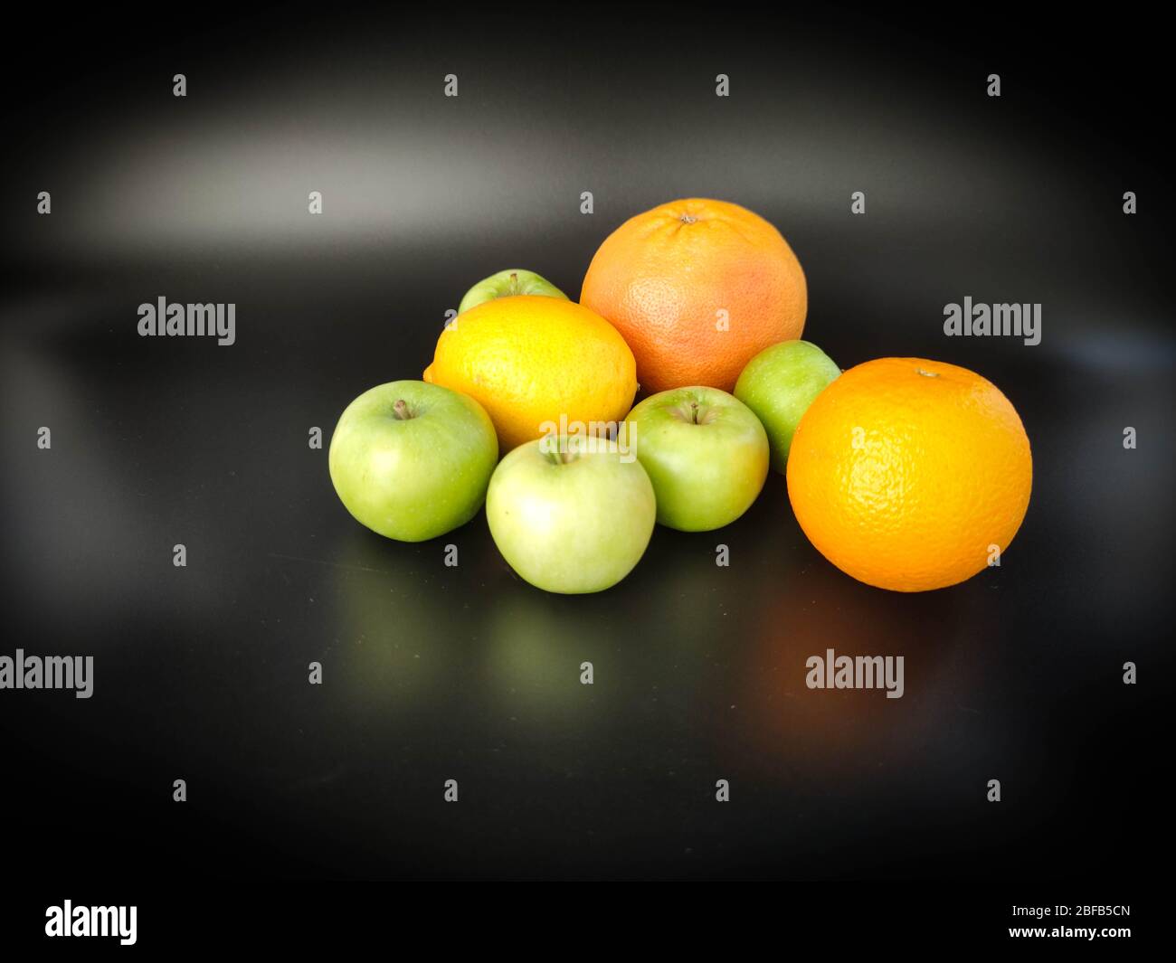 Whole fruits green apples, orange, grapefruit and lemon on black background. Concept - vegetarian and healthy food to improve the immunity Stock photo Stock Photo