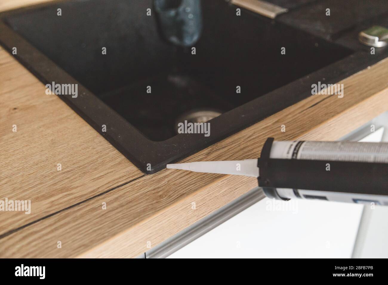 Man sealing kitchen sink joint between sink and countertop by silicone