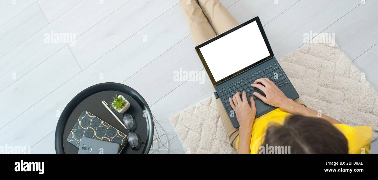 Top view of female freelancer sitting on floor near sofa at home and working on mockup laptop computer. Woman typing on laptop stay home. Quarantine Stock Photo