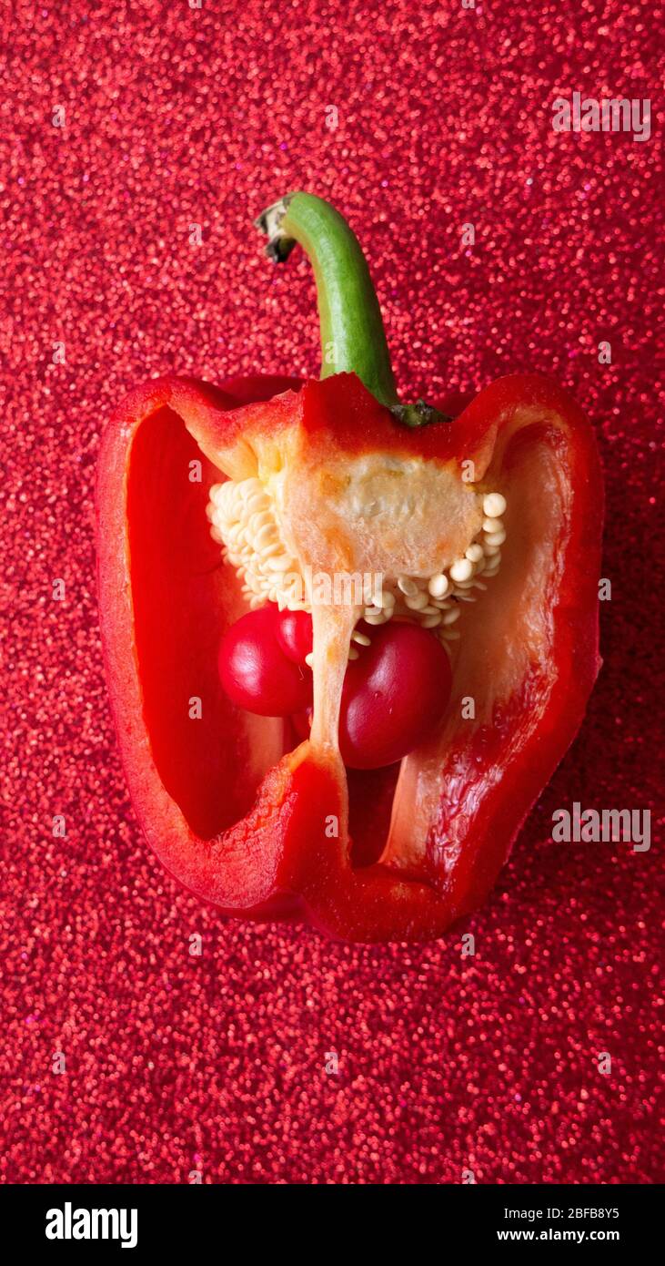 Two small bell peppers growing inside a red one, red glitter backdrop. Stock Photo