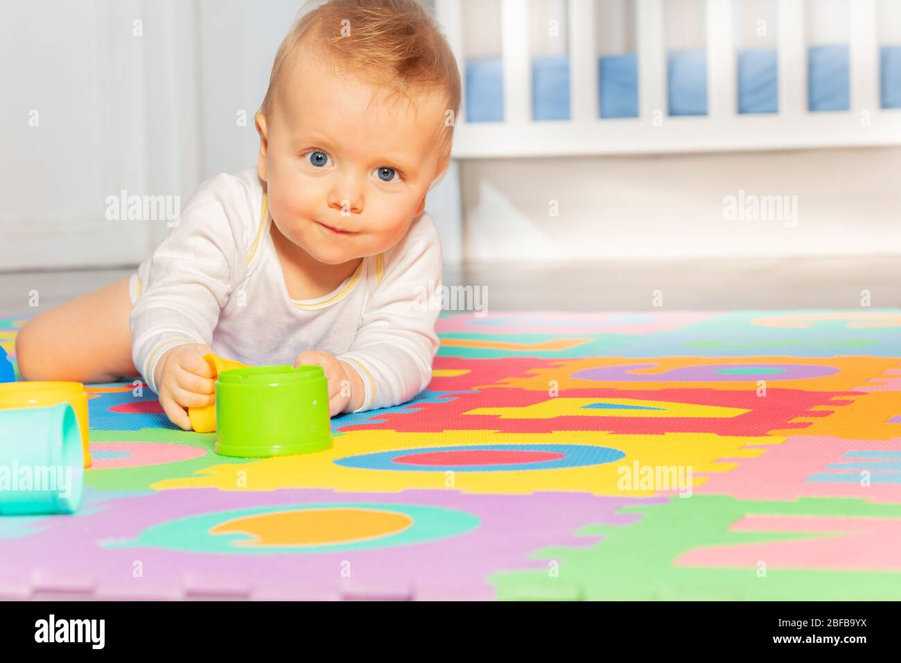 Beautiful baby toddler crawl on the floor of nursery grabbing toys near crib looking at camera