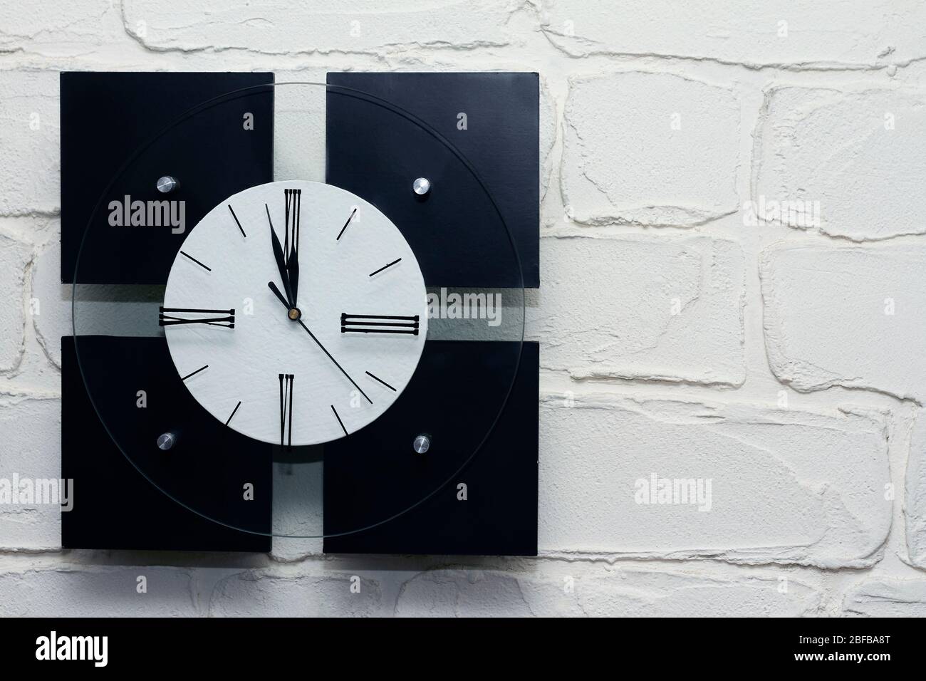 Square black and white clock on a white brick wall, background or concept Stock Photo