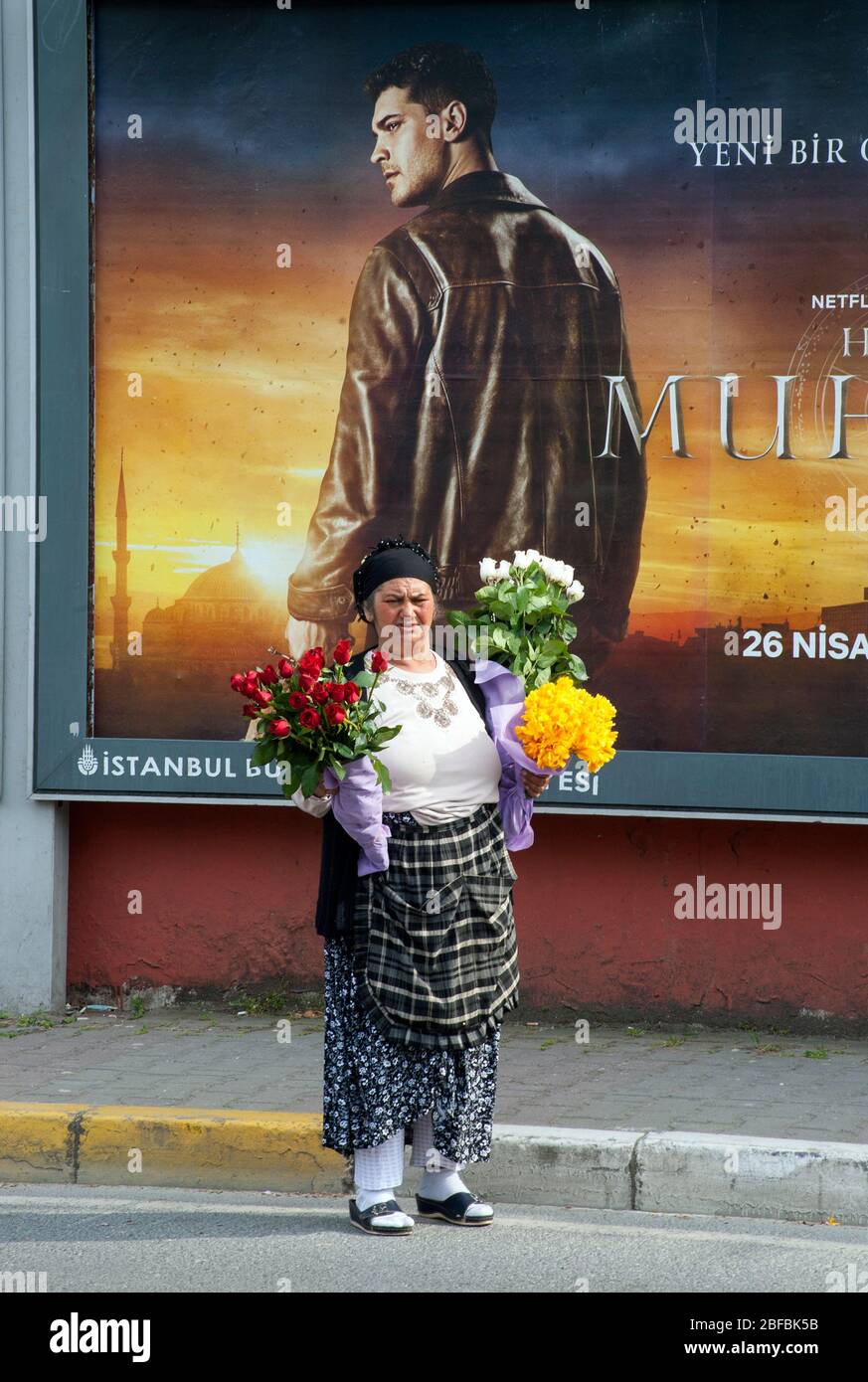 Gypsy woman selling flowers in front of outdoor advertising poster in streets of Istanbul, Turkey Stock Photo