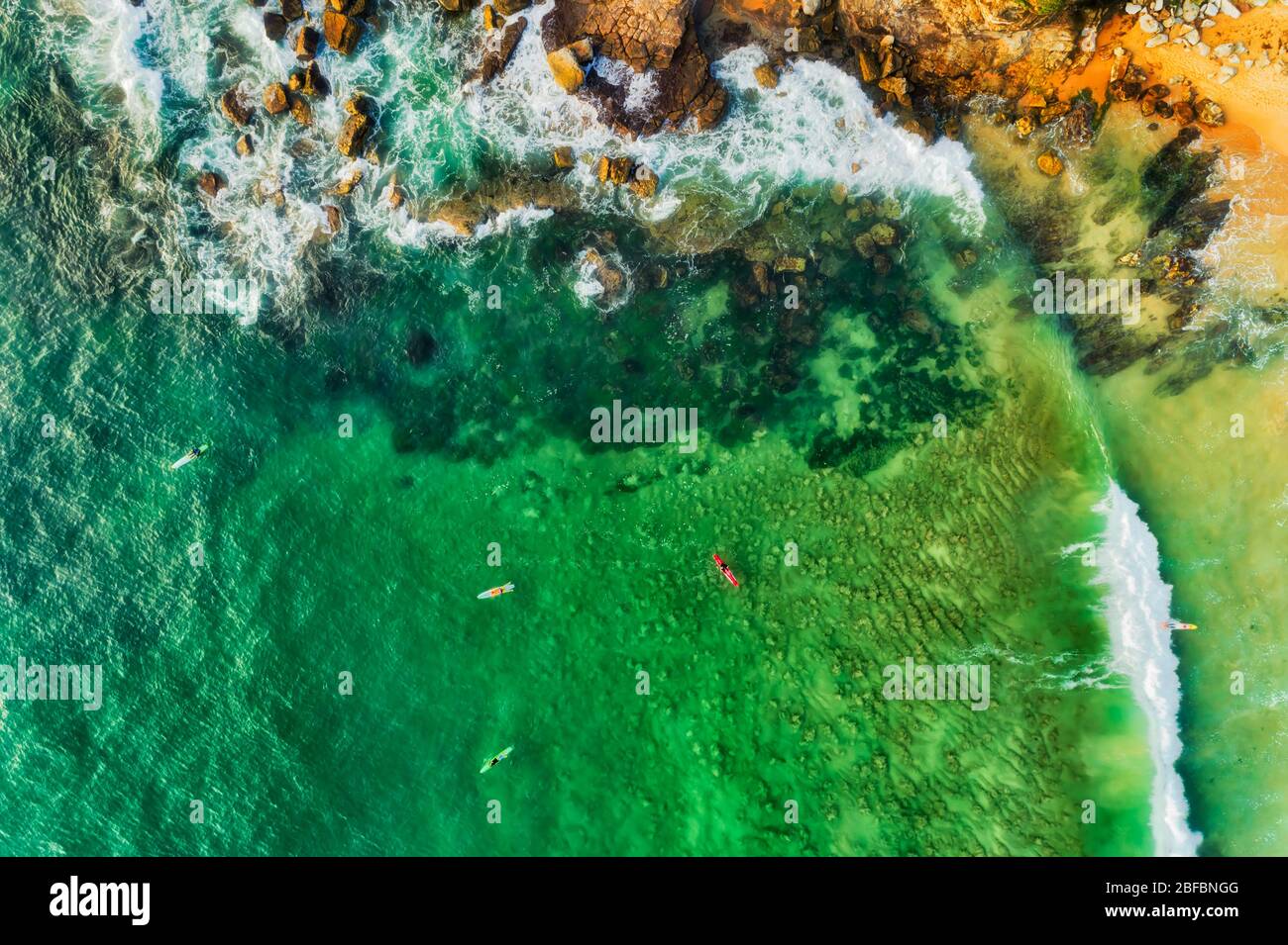 Top down aerial view of board surfers floating and riding the waves on Australian northern beaches. Stock Photo