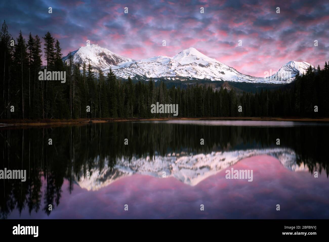 Last glow of autumn sunset over Central Oregon’s Three Sisters covered with fresh snowfall reflecting into Scott Lake and the Willamette National Fore Stock Photo