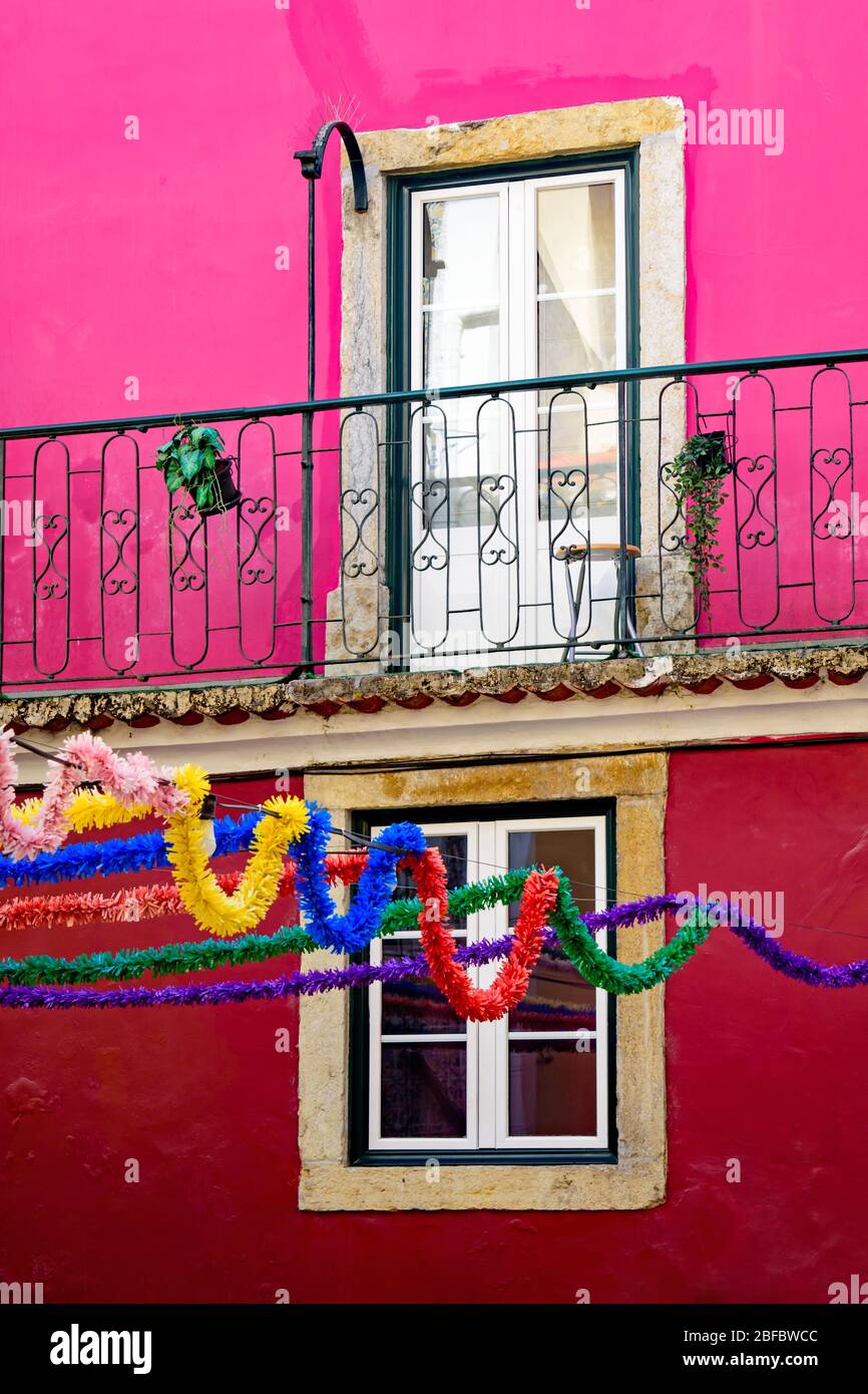 Colorful festival streamers hang in front of a fuschia colored building in the Alfama district of Lisbon Stock Photo