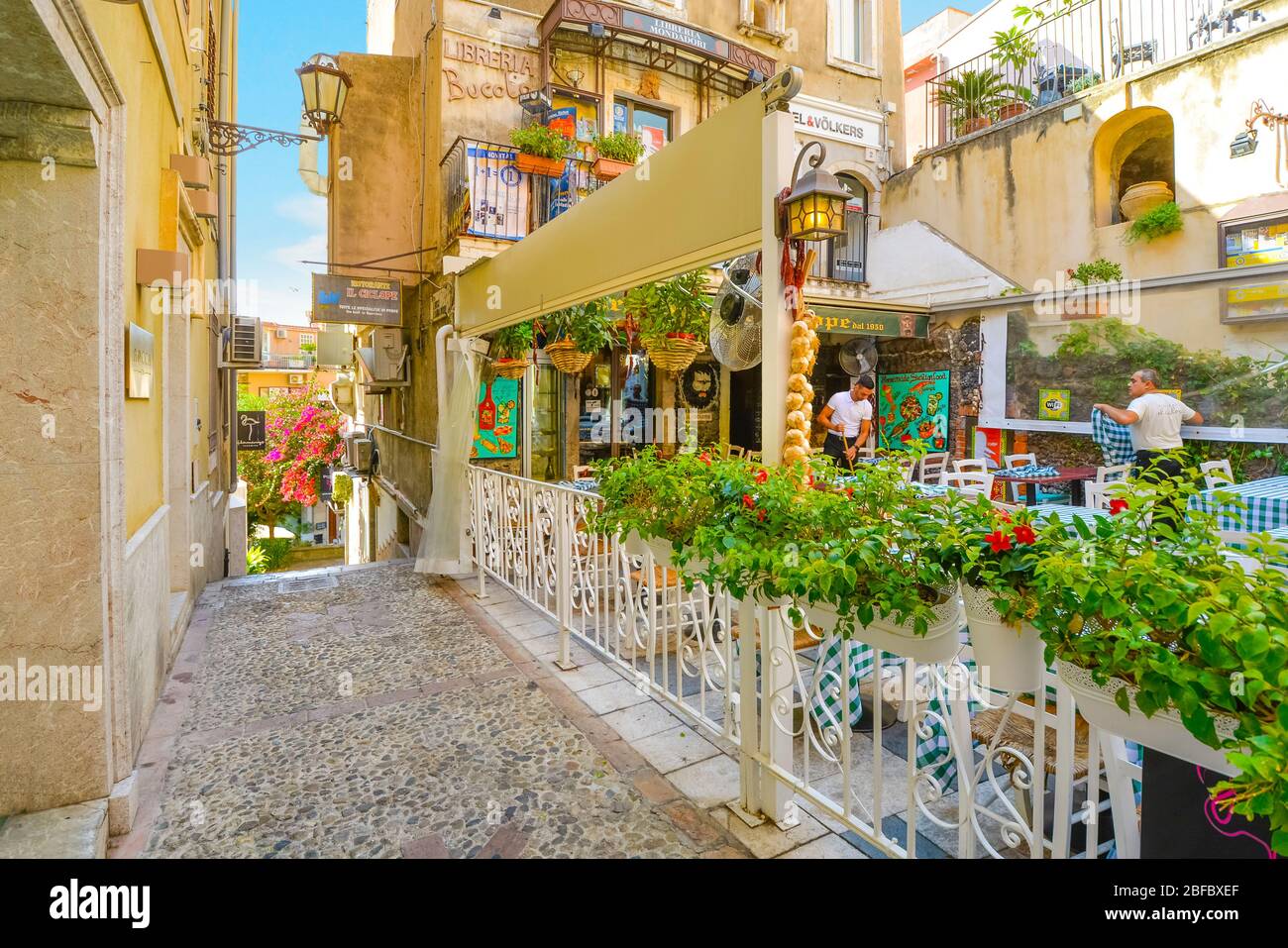 Workers prepare at a colorful Italian cafe restaurant along the touristic street through the resort town of Taormina, Italy, on the island of Sicily. Stock Photo