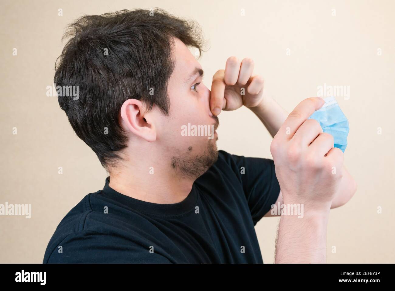 a young guy puts on a medical mask. Hands clamped over his nose. It is important to wear a mask during the risk of infection. Medical concept. Stock Photo