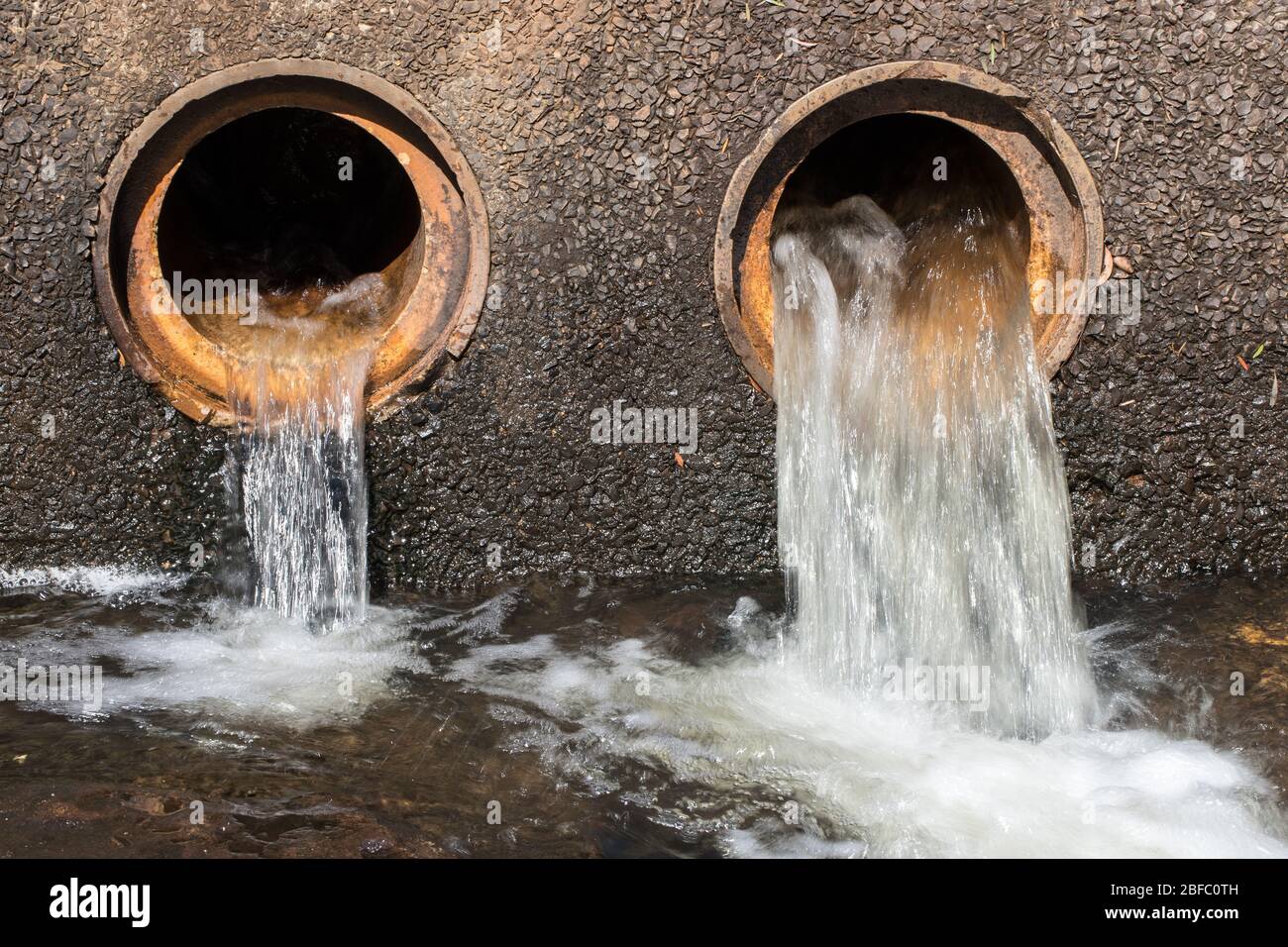 Water flowing from pipes under causeway on road Stock Photo