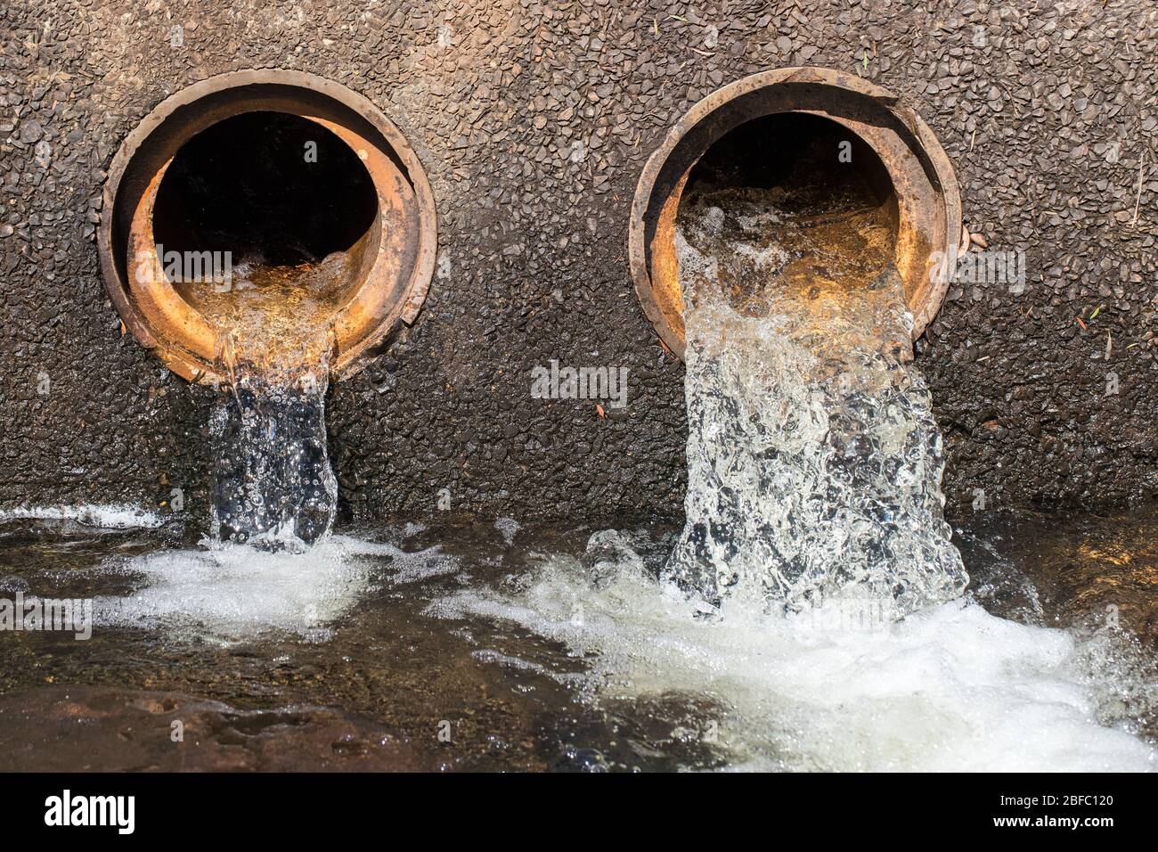 Water flowing from pipes under causeway on road Stock Photo