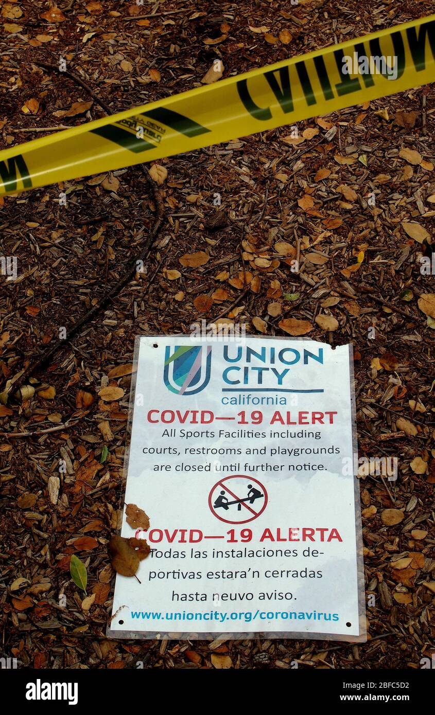 Covid-19 alert sign on ground at exercise area closed off with yellow caution tape  in Cann Park in Union City, due to covid-19 virus pandemic, California Stock Photo