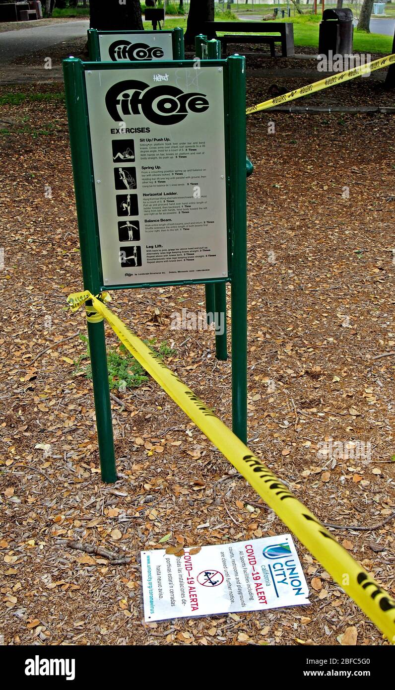 Covid-19 alert sign on ground at exercise area closed off with yellow caution tape  in Cann Park in Union City, due to covid-19 virus pandemic, California Stock Photo