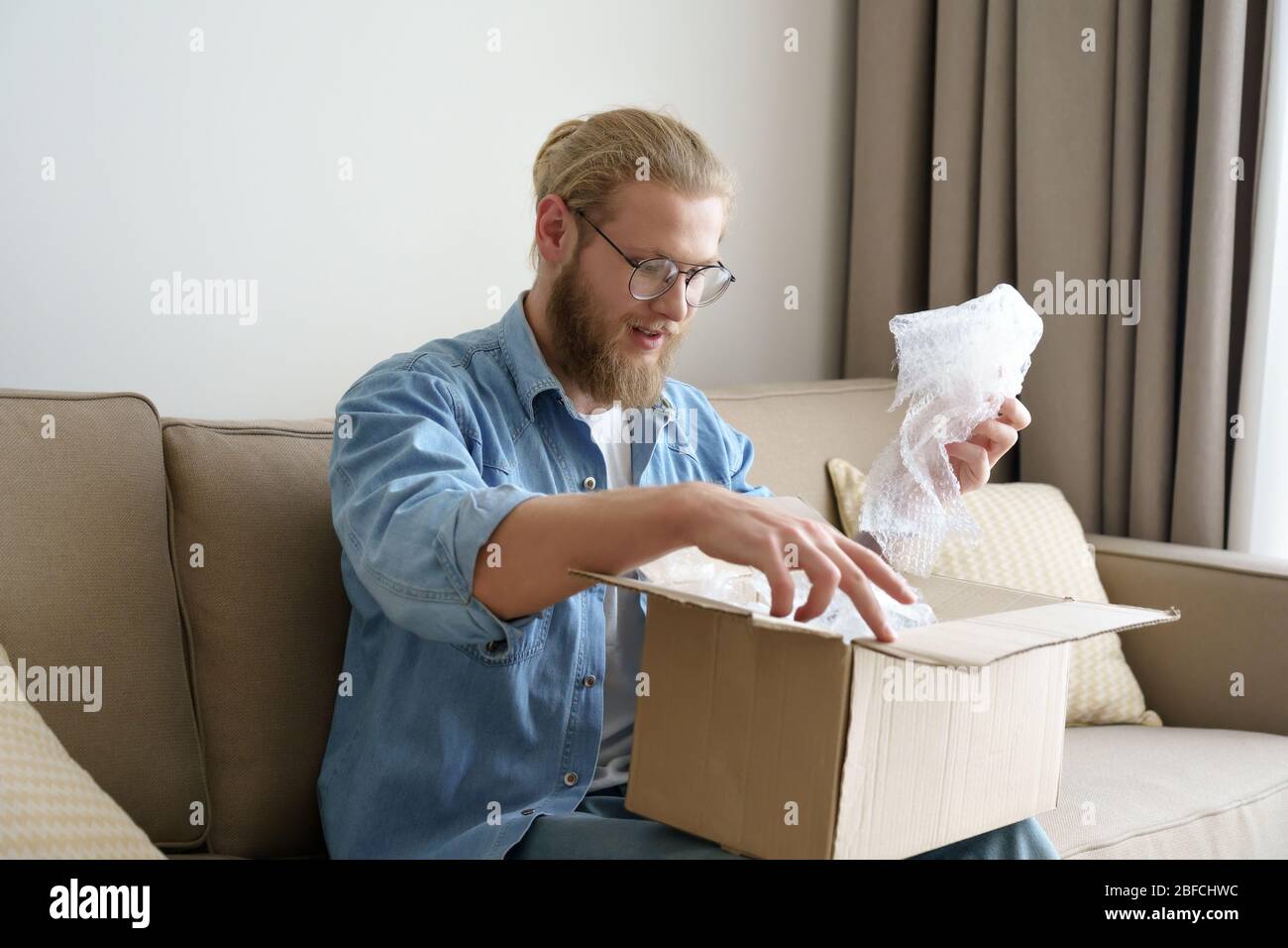 Happy man customer open cardboard box unpacking post mail delivery package. Stock Photo