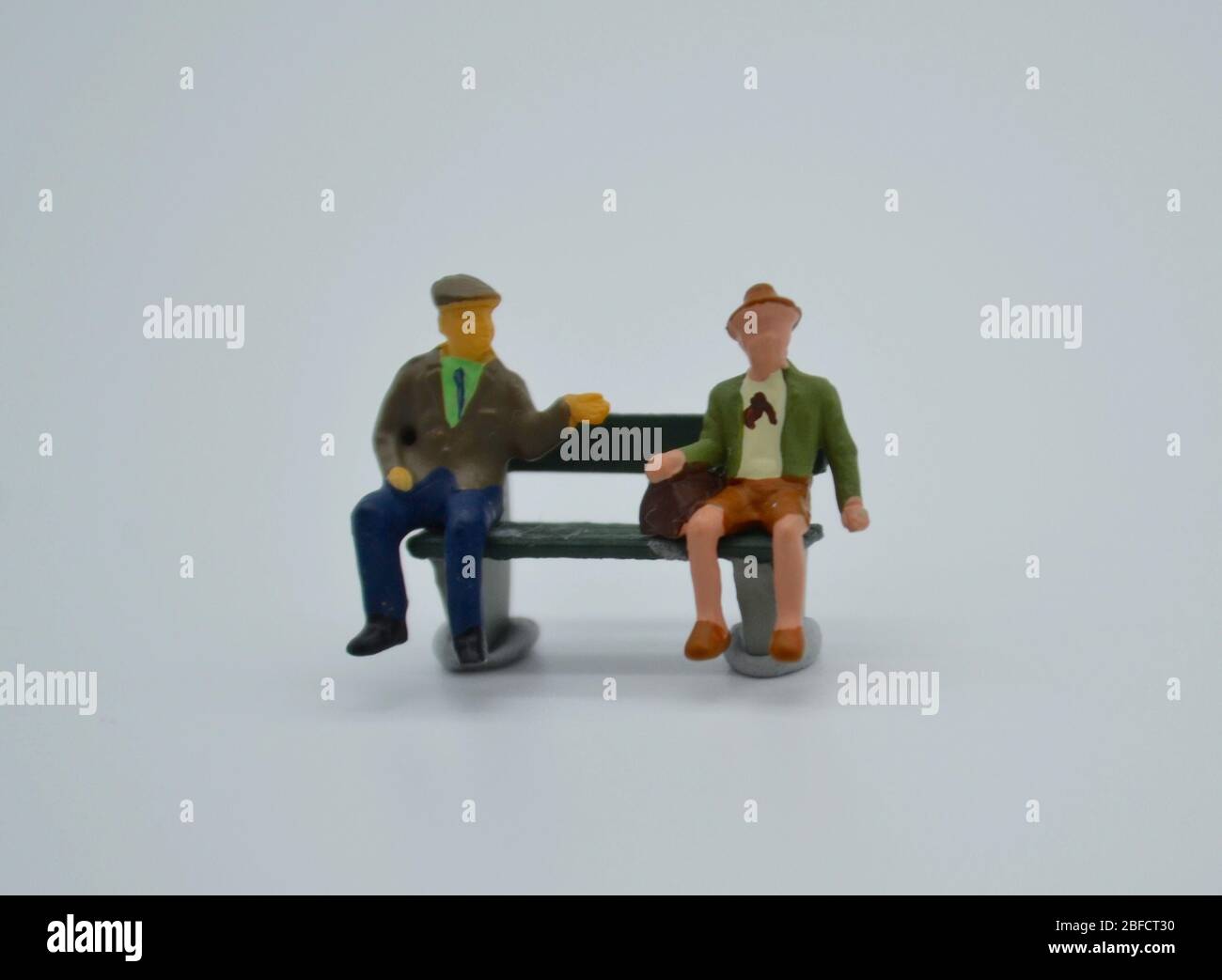 Miniature figurine scene with two old men on a park bench practicing social distancing in the time of the COVID 19 pandemic Stock Photo