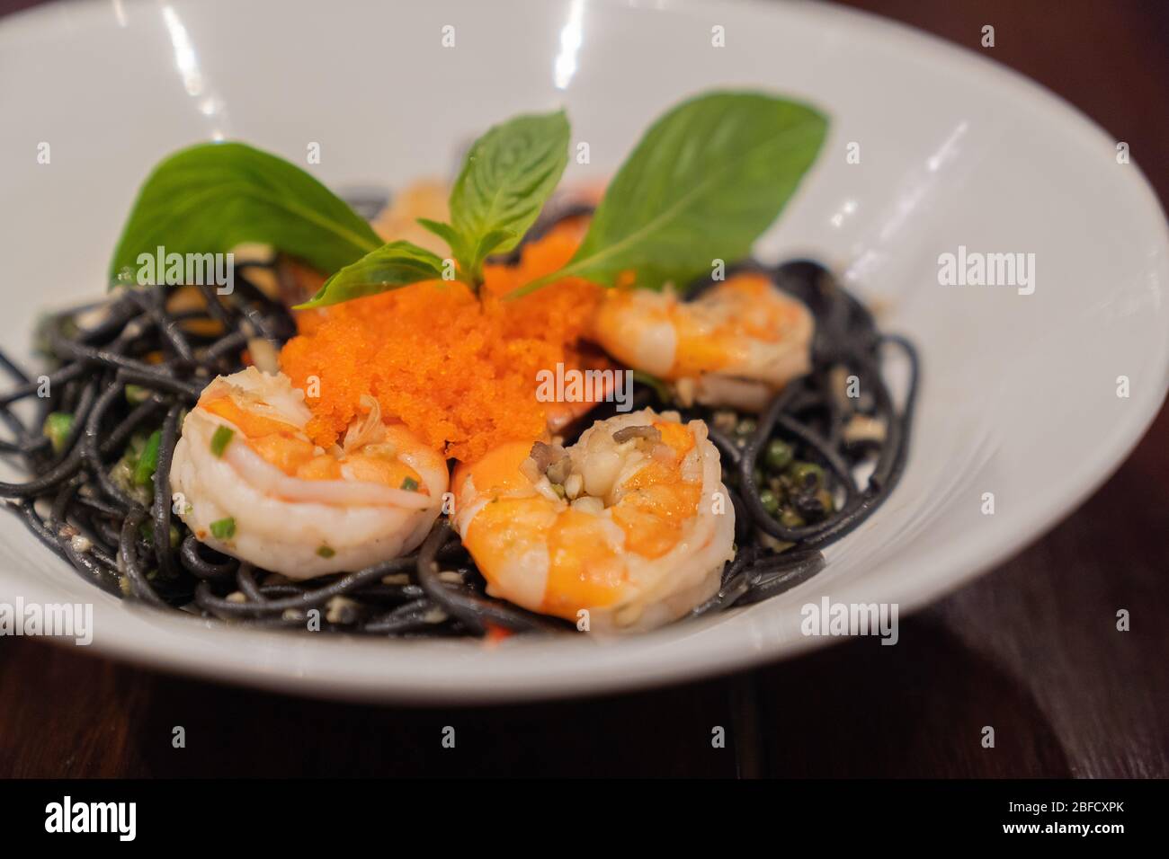 Close up. Black Spaghetti sea food with big shrimp and egg fish on white dish, on wood table. Italian food. Italy food style. Top view. Stock Photo