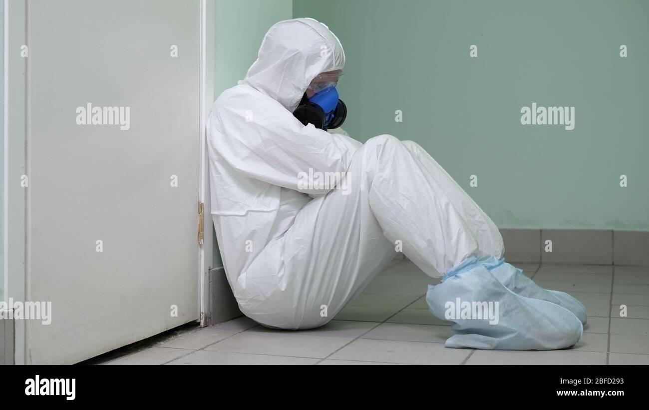 Medium shot. Tired doctor in hazard suit sitting and sleeping on the floor. Overworked doctor. Professional shot in 4K resolution. 054. You can use it Stock Photo