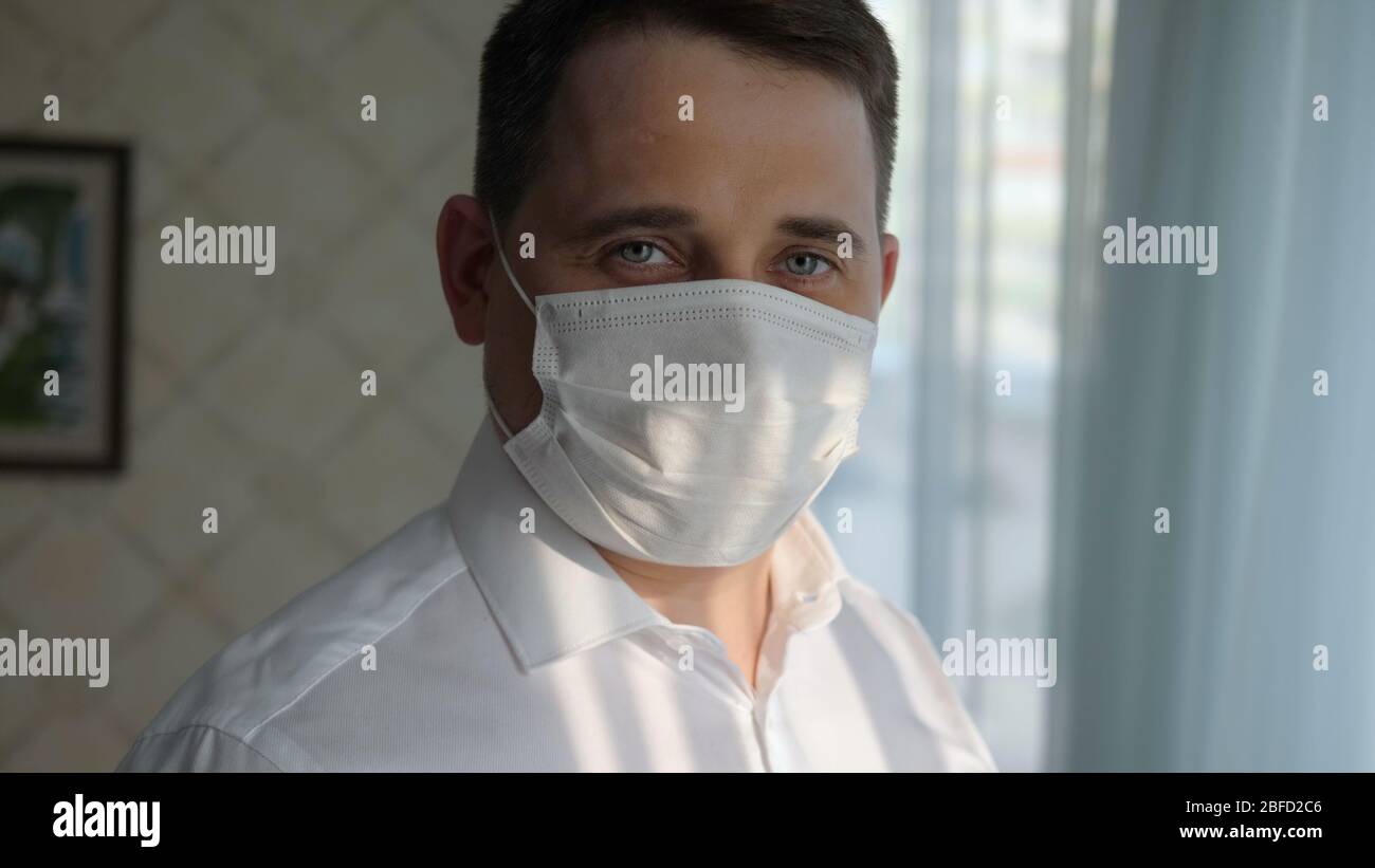 Close up. Confident business man in a medical mask at home looking to camera. Professional shot in 4K resolution. 054. You can use it e.g. in your com Stock Photo