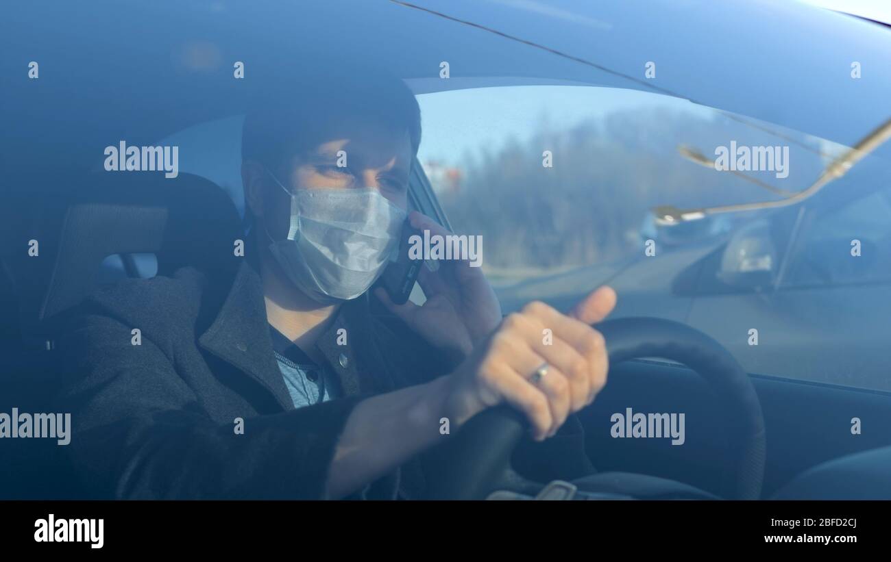 Medium shot. Businessman in medical face mask using mobile phone inside car. Professional shot in 4K resolution. 054. You can use it e.g. in your comm Stock Photo