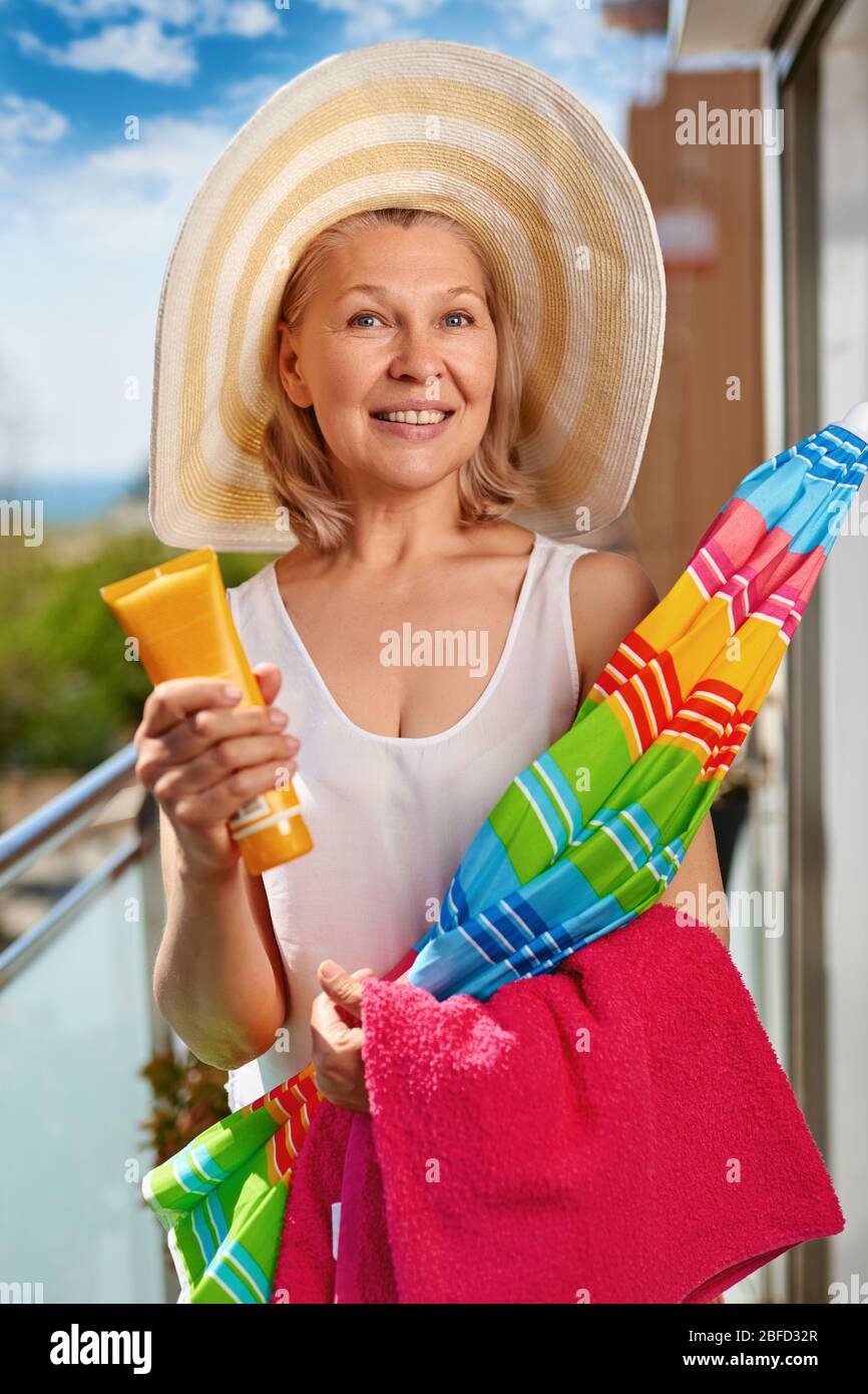 Mature tourist woman in hat with beach accessories in hand on balcony ...