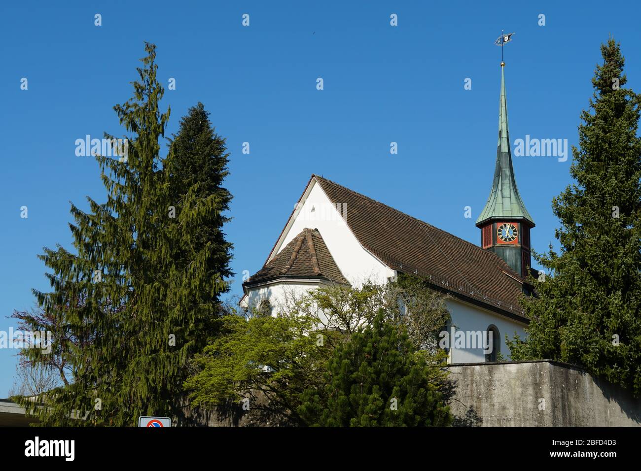 Old reformed church building in Urdorf, Switzerland surrounded by trees, lateral view with detail of the church tower on a clear day in spring. Stock Photo