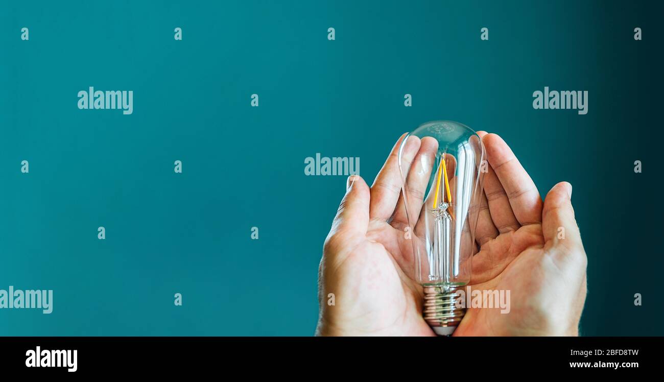 Two hands holding a light bulb on a green background with copy space ...
