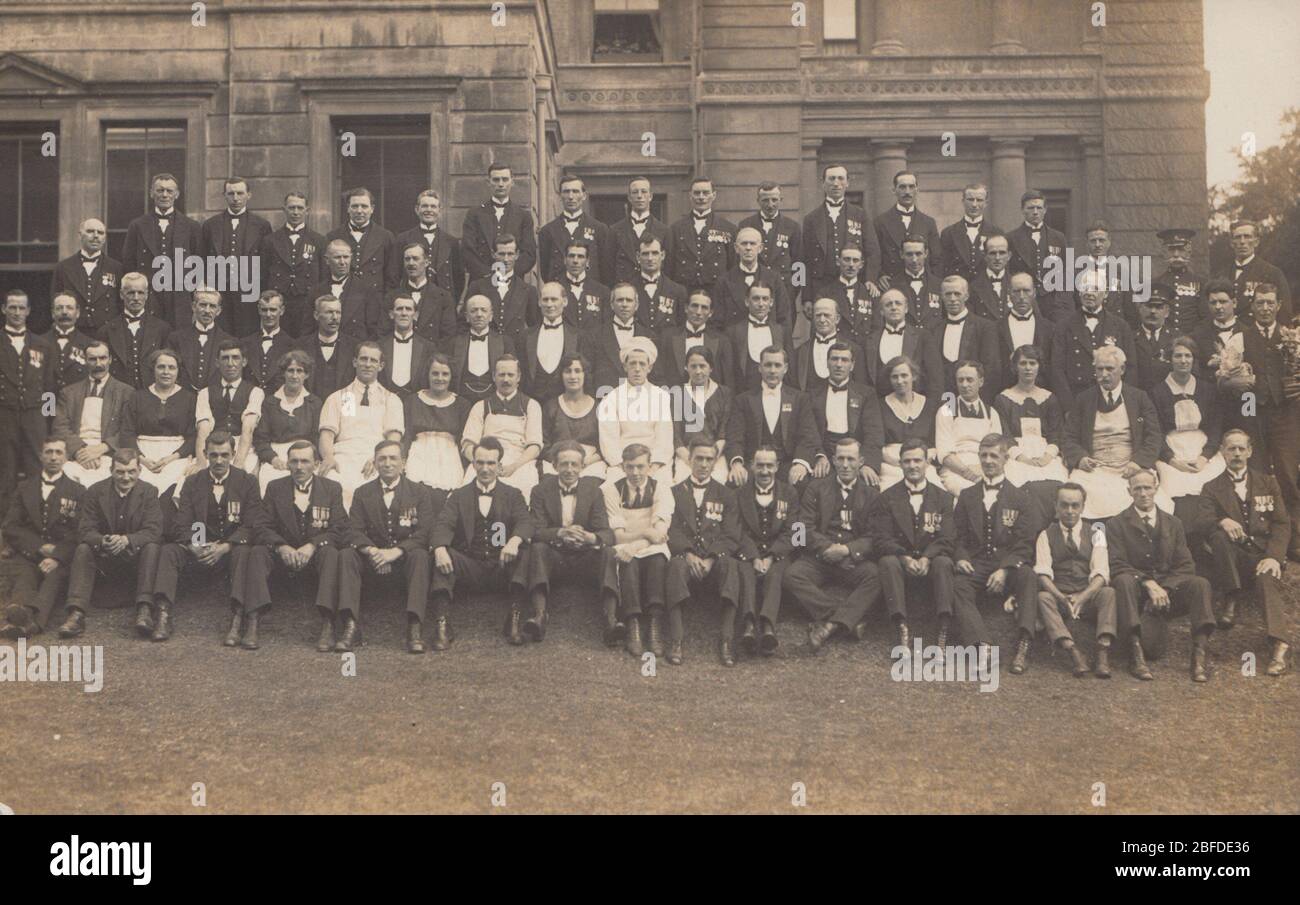 Vintage Early 20th Century British Photographic Postcard Showing a Large Group of Men Wearing Medals Posing With Catering Staff. Posing Outside a Grand Building. Stock Photo