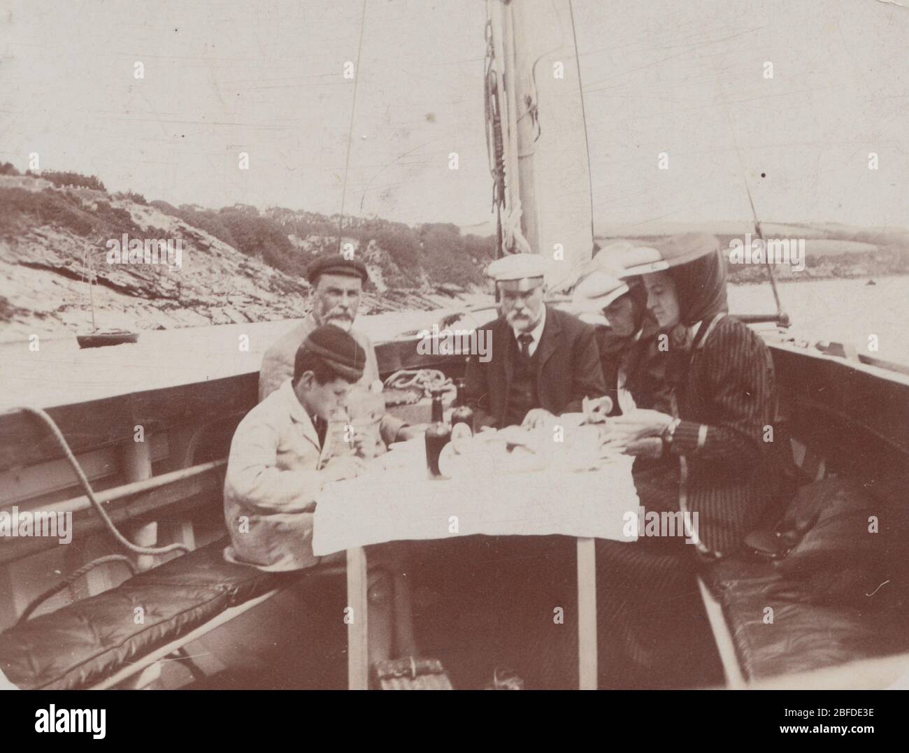 Vintage Edwardian Photographic Postcard Showing a Sailor and His Companions Having Drinks On-board a Sailing Vessel Known as a Quay Punt. Having Lunch on The Helford River. Posted From Falmouth in Cornwall in 1909. Stock Photo
