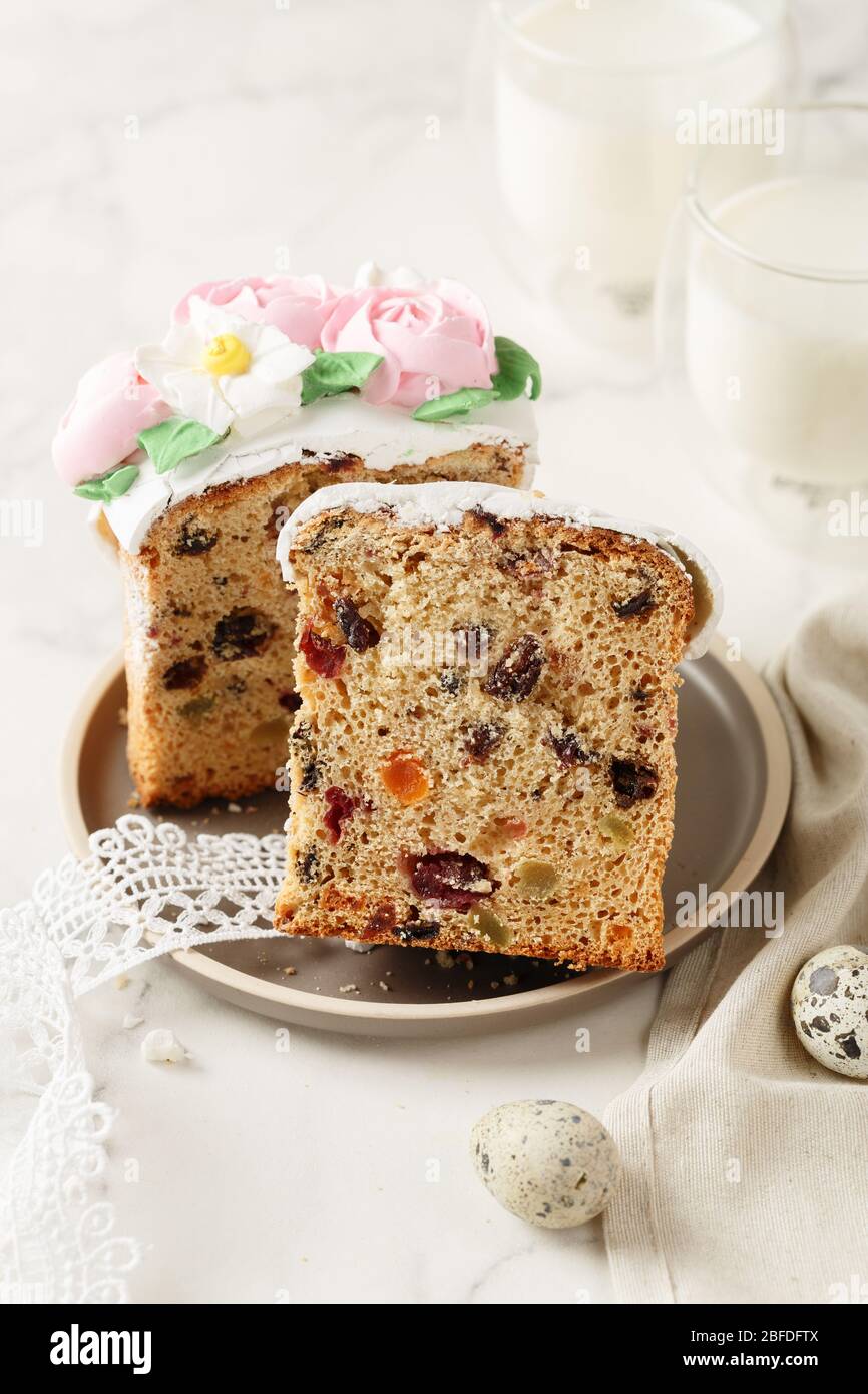 Slice of Easter cake with raisins and dried apricots. Homemade pie with a glass of milk. Piece of cake with marzipan floral decoration on plate. Holid Stock Photo