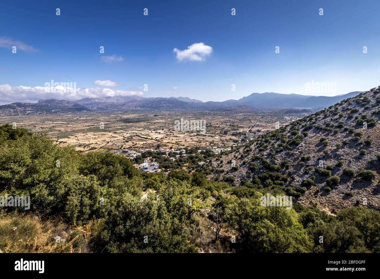 Top view of the Lassithi Plateau on a sunny clear day with trees in the foreground and a cloudy sky in the background. Crete island, Greece. Stock Photo