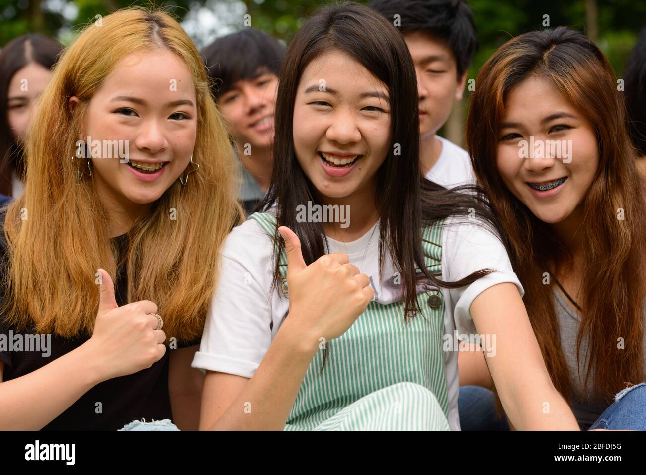 Happy young group of friends giving thumbs up together at the park ...